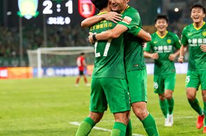 北京国安球员在进球后拥抱庆祝，背景是记分牌显示2比1的比分，绿色草坪上球员们情绪激动